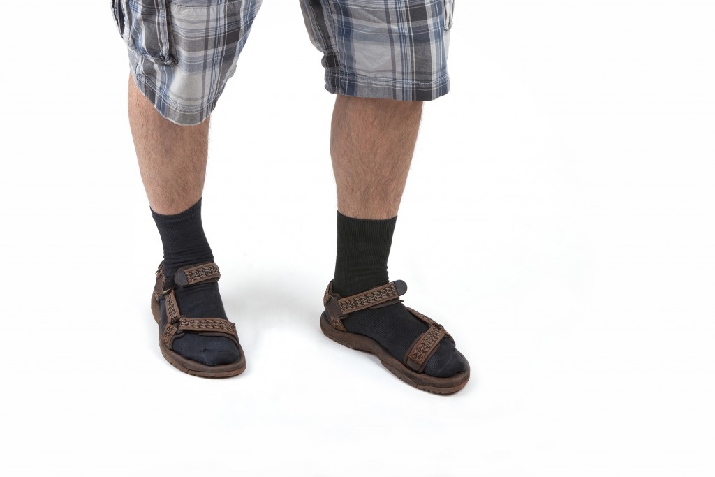 studio shot of a man wearing sandals with socks and having hairy legs, isolated on white.