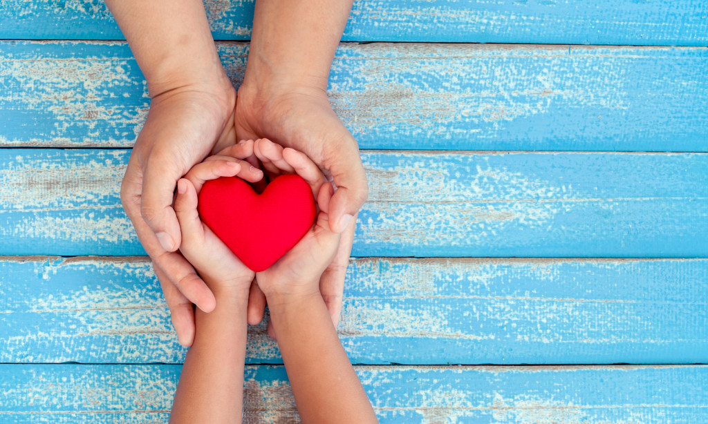 Red heart in child kid and mother hands on old blue wooden table in vintage retro style